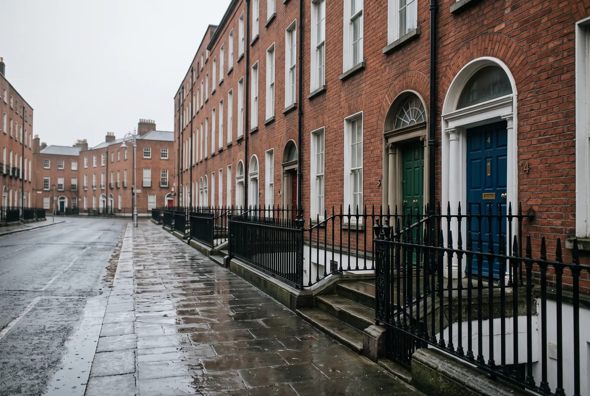 A terrace of red-brick Georgian houses on a wet Dublin street, with painted front doors, fanlights and black iron railings